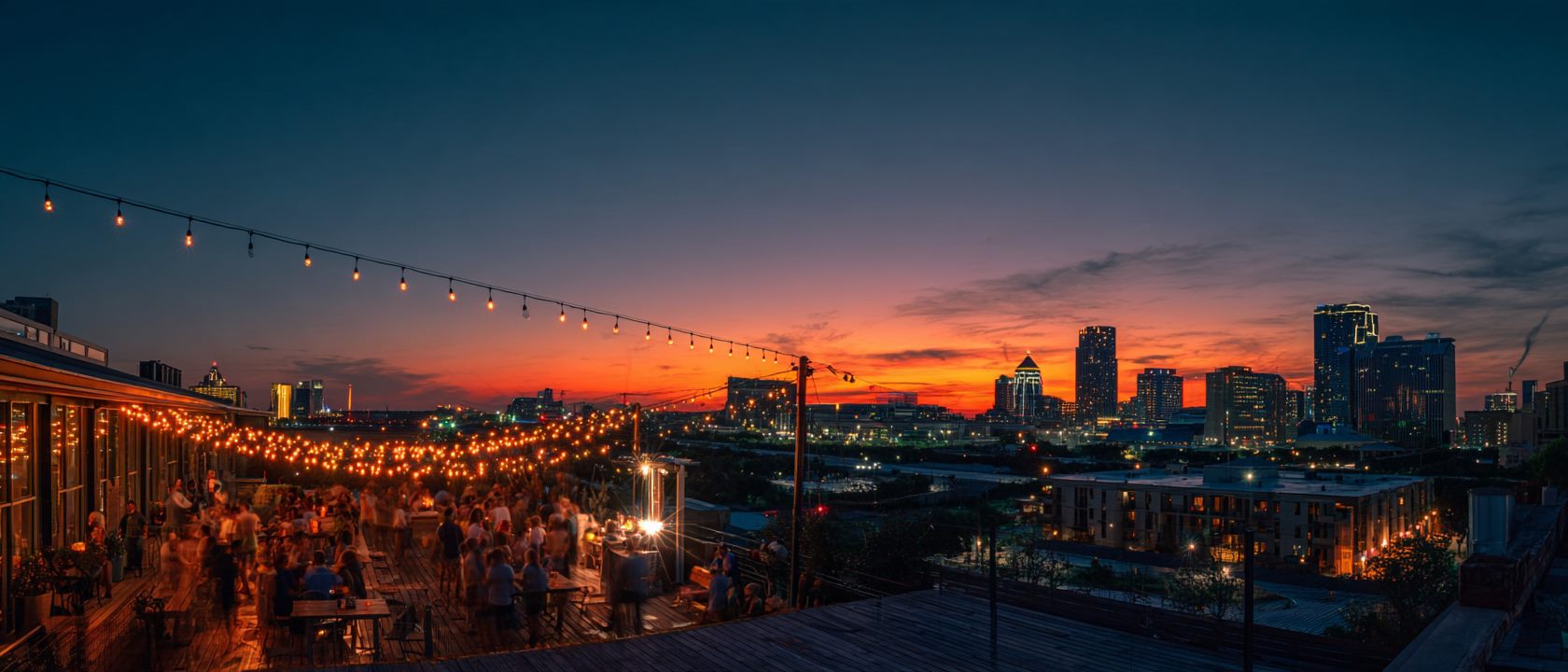 A rooftop party under string lights with the Dallas skyline glowing at sunset